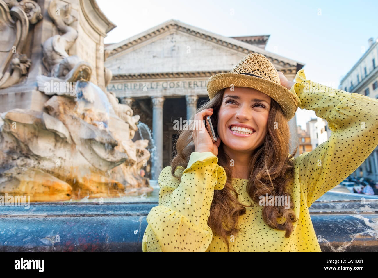 Tenendo il suo cappello, una felice brunette sorrisi mentre si parla al telefono vicino al Pantheon fontana di Roma. Foto Stock