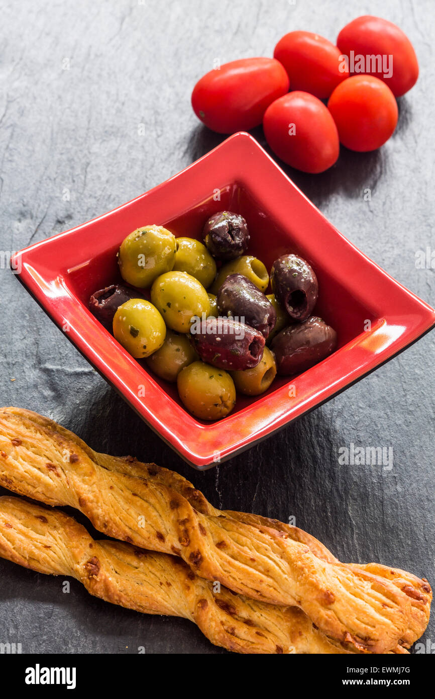 Olive misti in un quadrato rosso il piatto con il formaggio gruviera e papavero grissini e pomodori in ardesia Foto Stock