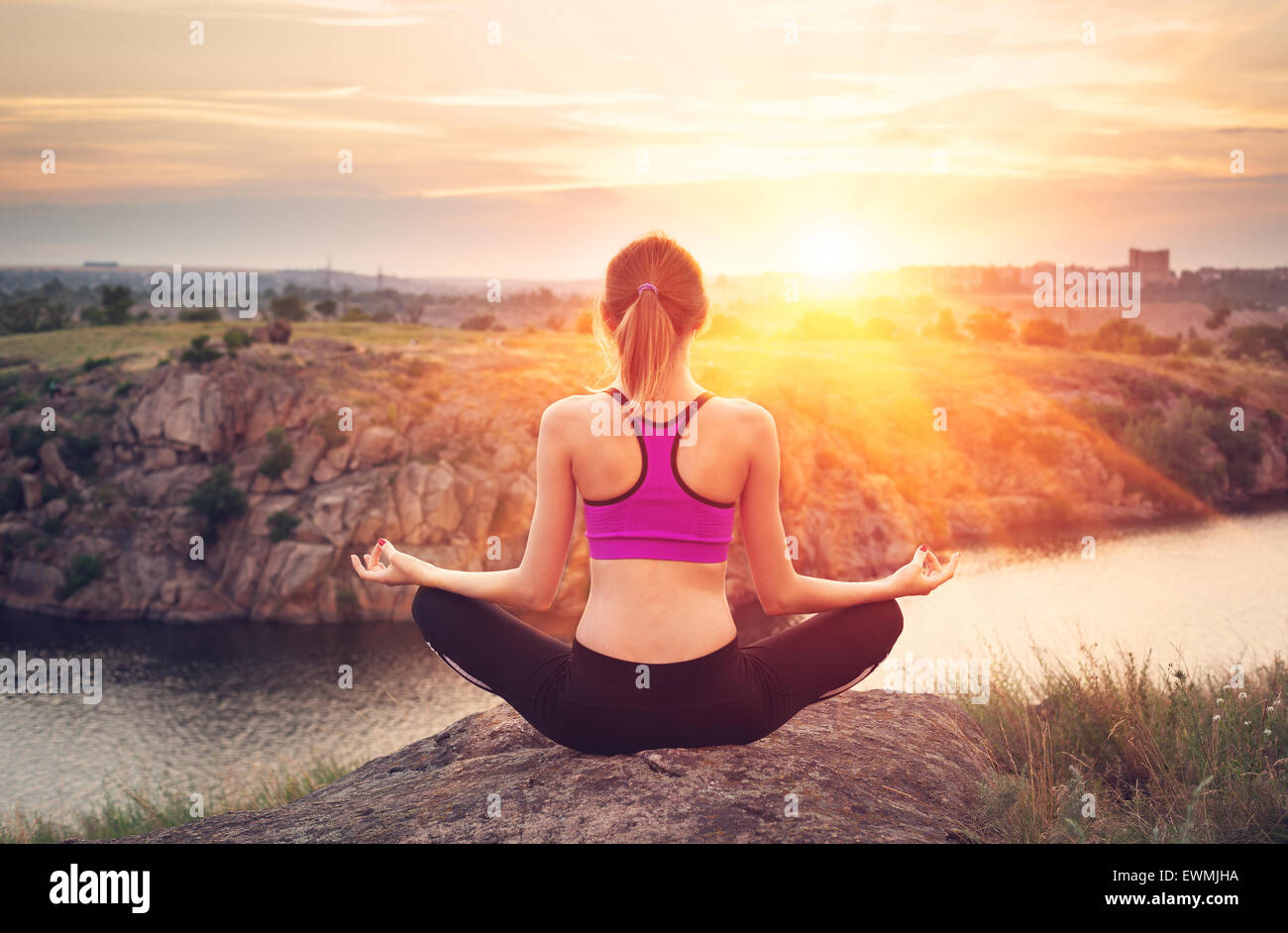 Giovane donna a praticare yoga sulla collina al tramonto vicino al fiume. Foto Stock