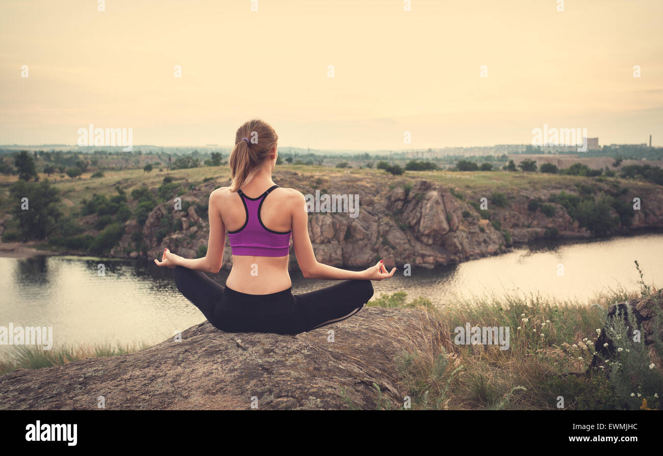 Giovane donna a praticare yoga sulla collina al tramonto vicino al fiume. Foto Stock