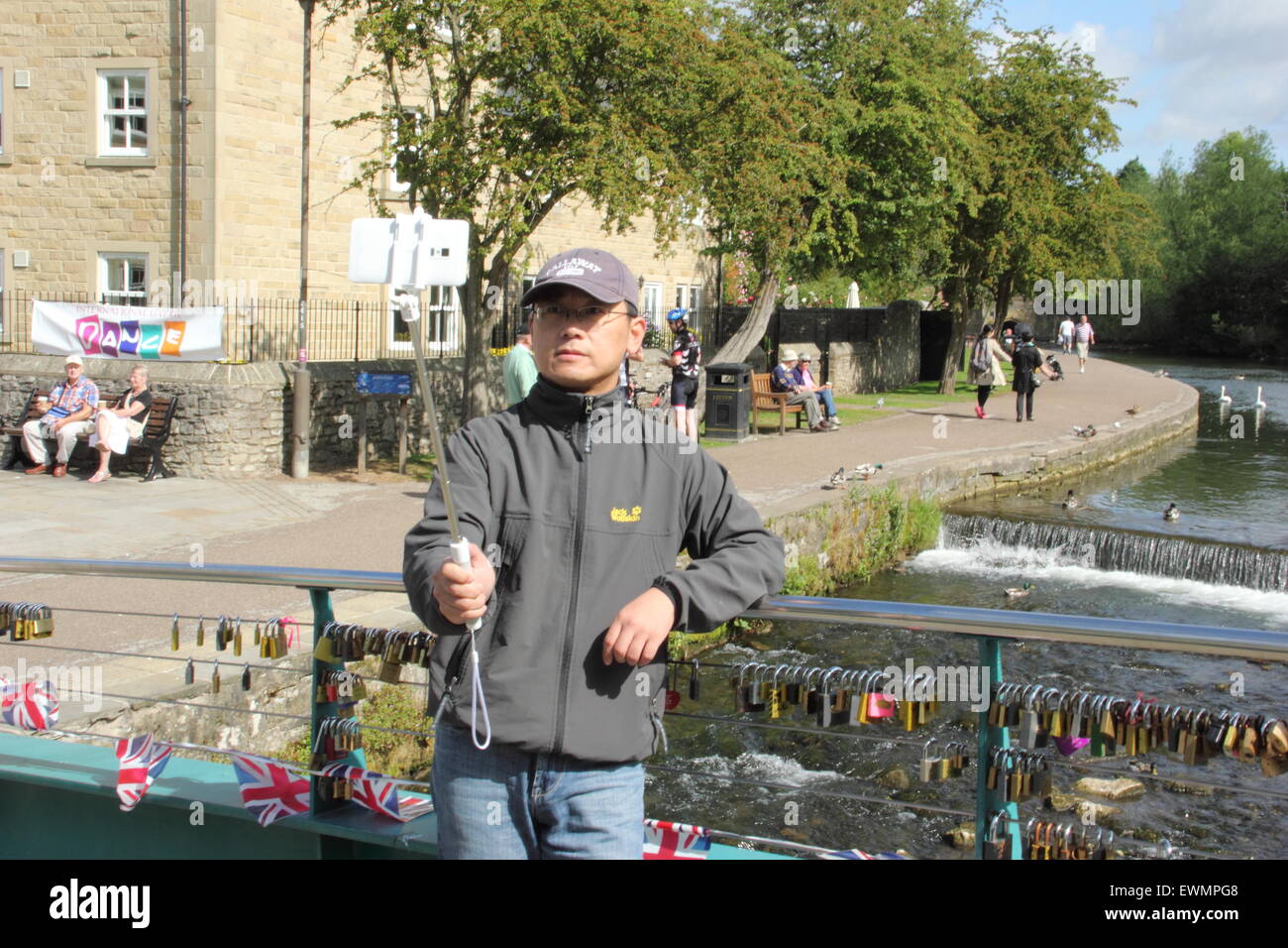 Un uomo prende una fotografia di se stesso con un 'selfie stick' su un ponte in Bakewell, Peak District Derbyshire England Regno Unito Foto Stock
