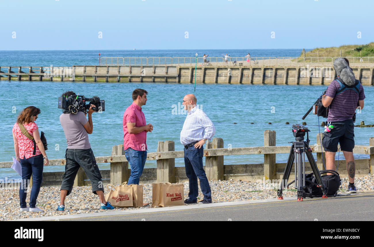 Gregg Wallace e Chris Bavin filmata per il mangiare bene per meno TV show su una spiaggia in riva al mare. Foto Stock