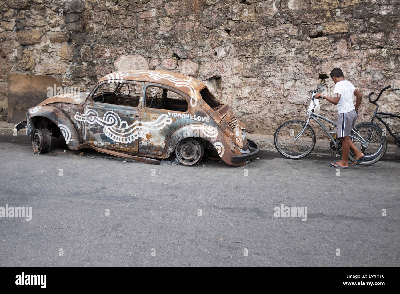 RIO DE JANEIRO, BRASILE - MARZO 07, 2015: Brasiliano uomo spinge la bicicletta un passato vandalizzato fusca auto in favela Vidigal. Foto Stock