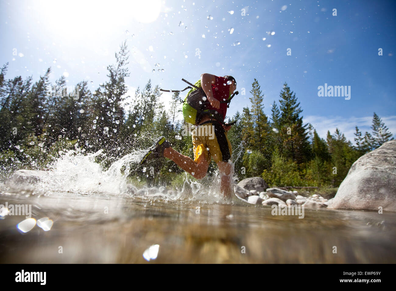 Giovane uomo adulto in esecuzione attraverso un piccolo fiume con un super leggero zaino Foto Stock