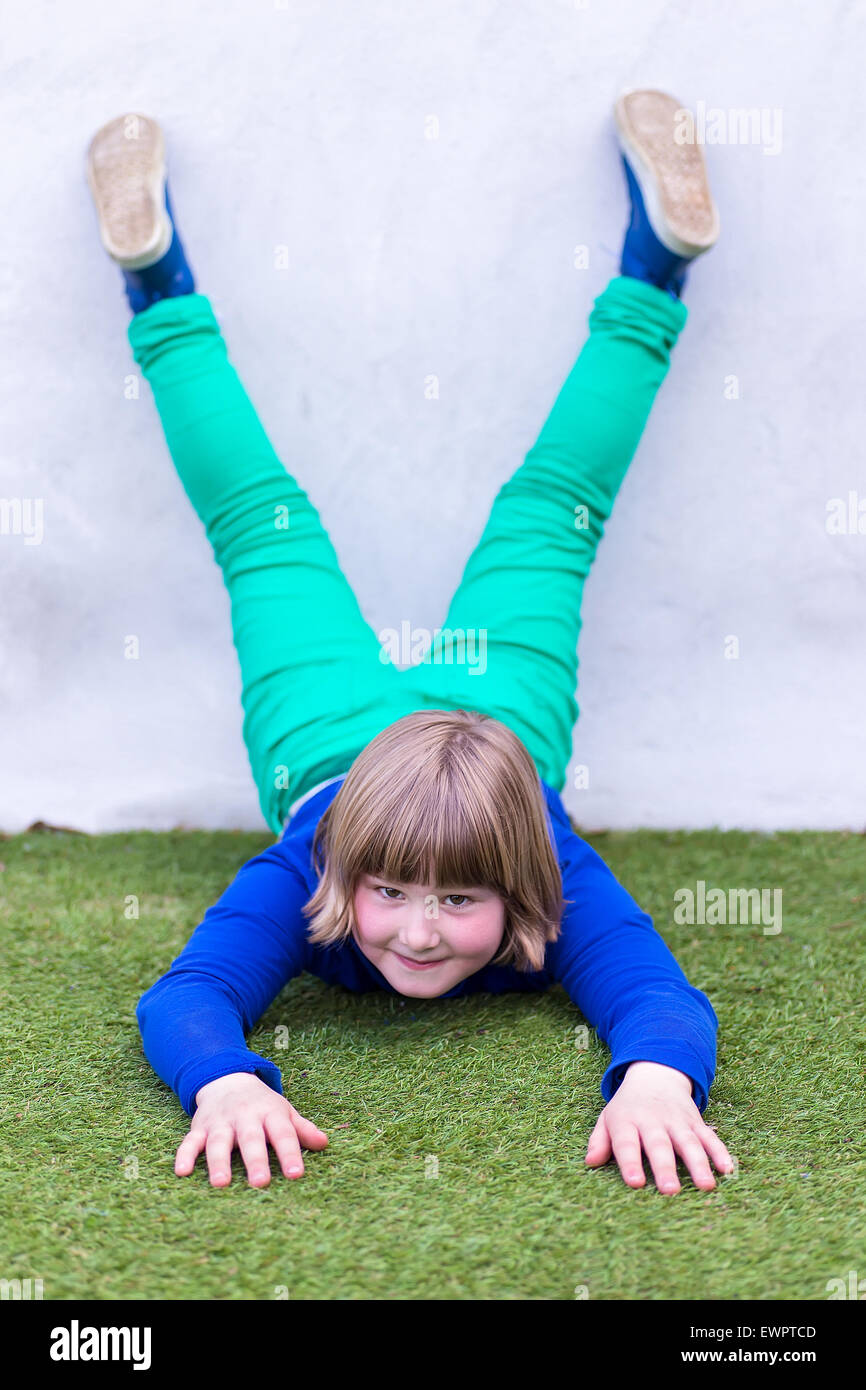 Giovane ragazza caucasica giacente capovolto contro la parete sull'erba al parco giochi Foto Stock
