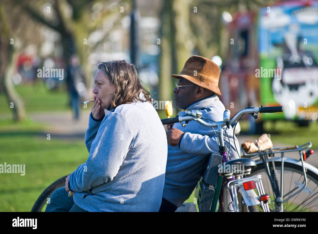 Un uomo nero e una donna bianca a sedersi su una panchina in un parco di Londra a guardare il mondo che passa da mentre lei ha una sigaretta Foto Stock