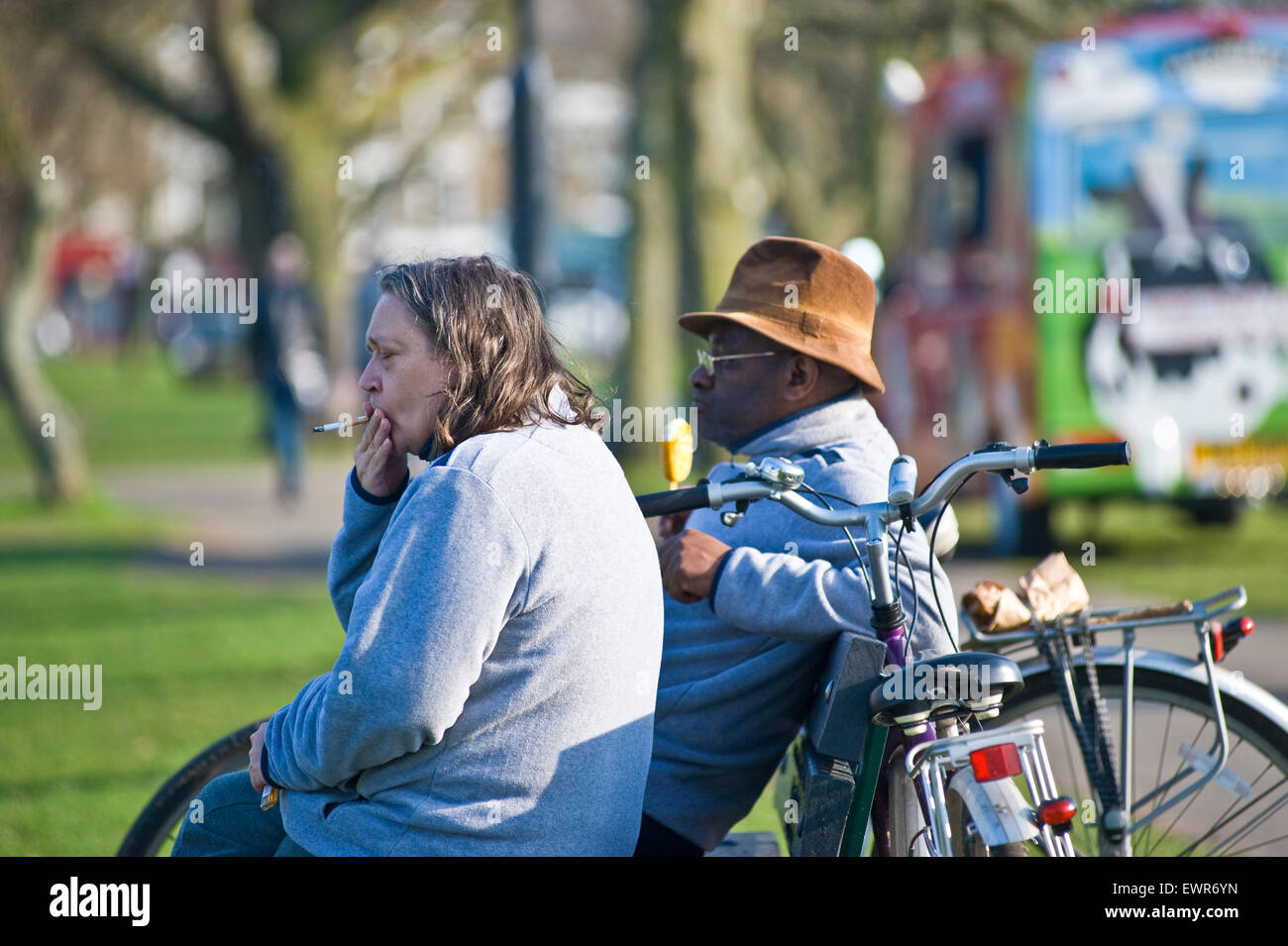 Un uomo nero e una donna bianca a sedersi su una panchina in un parco di Londra a guardare il mondo che passa da mentre lei ha una sigaretta Foto Stock
