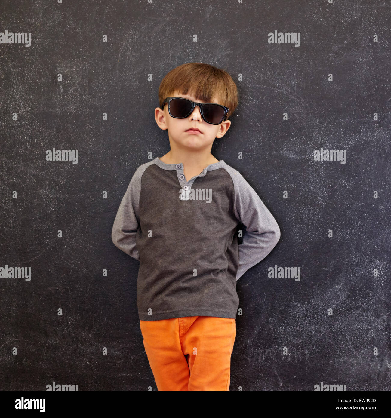 Carino piccolo bambino in piedi di fronte a una lavagna. Elegante piccolo ragazzo che indossa gli occhiali da sole appoggiata su una lavagna guardando ca Foto Stock