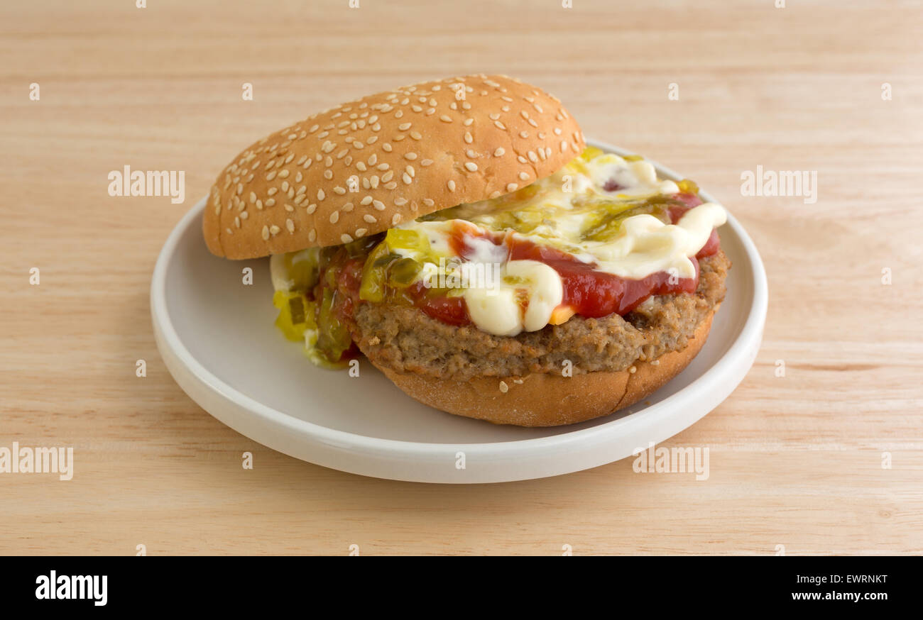 Un cheeseburger con semi di sesamo bun plus maionese, ketchup e assaporare una piccola piastra in cima al tavolo di legno. Foto Stock