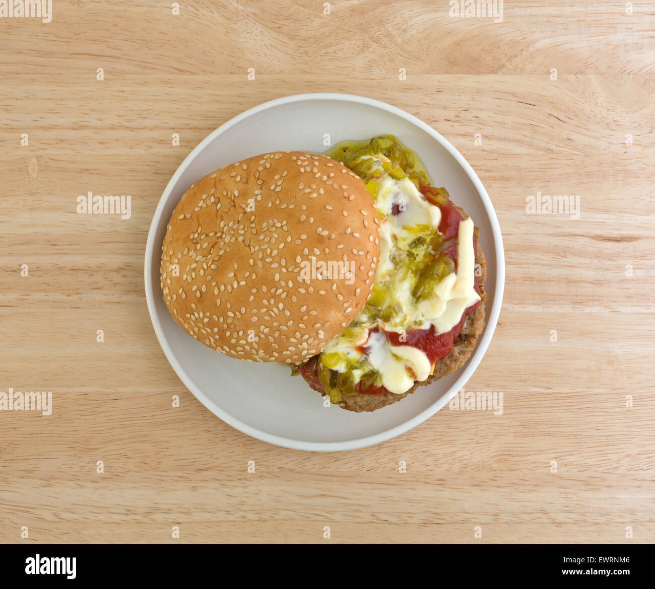 Vista dall'alto di un cheeseburger con semi di sesamo bun plus maionese, ketchup e assaporare una piccola piastra in cima al tavolo di legno. Foto Stock