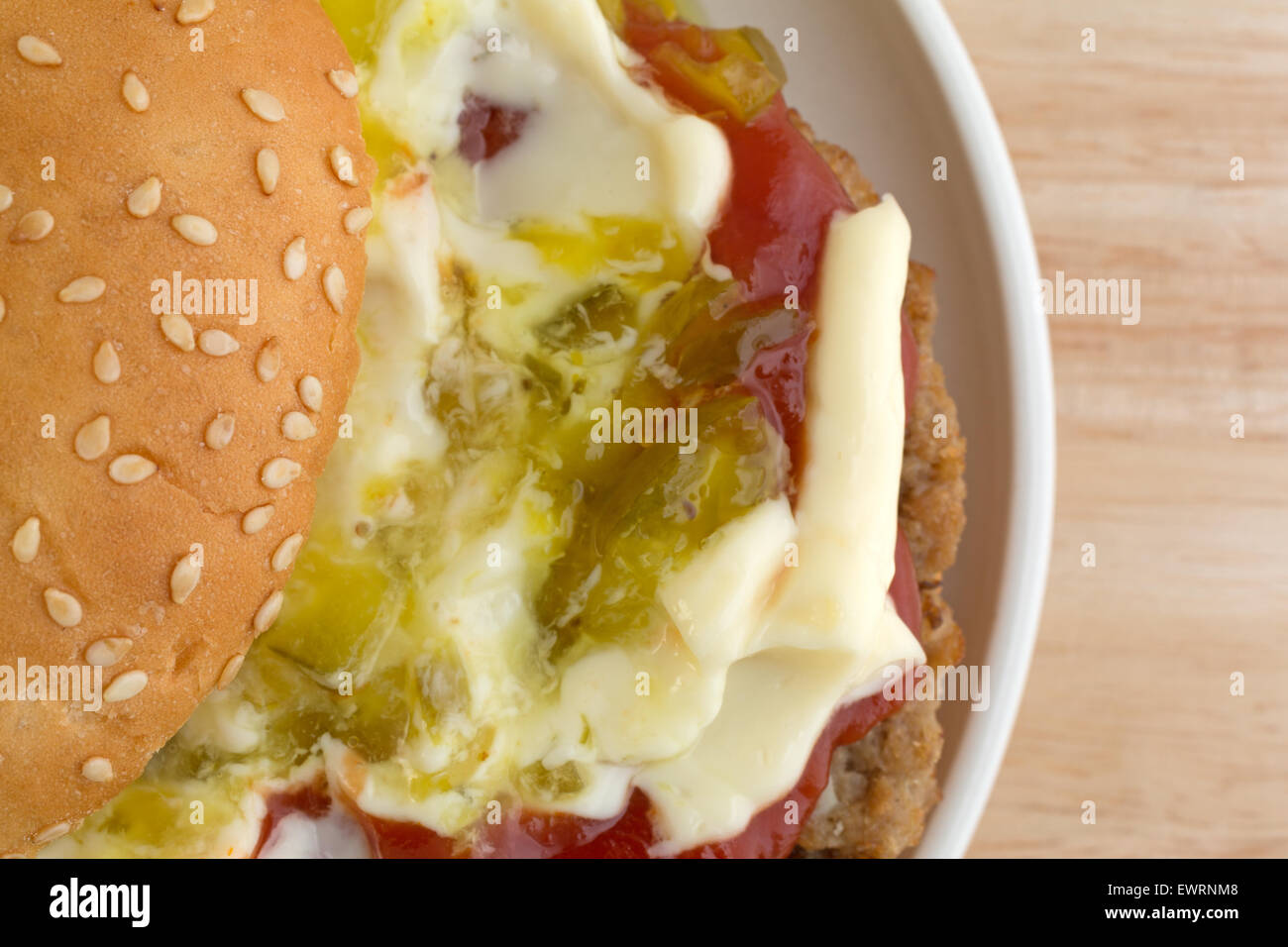 Top vista ravvicinata di un cheeseburger in un seme di sesamo bun coperto con la maionese, ketchup e assaporare una piccola piastra in cima scheda di legno Foto Stock