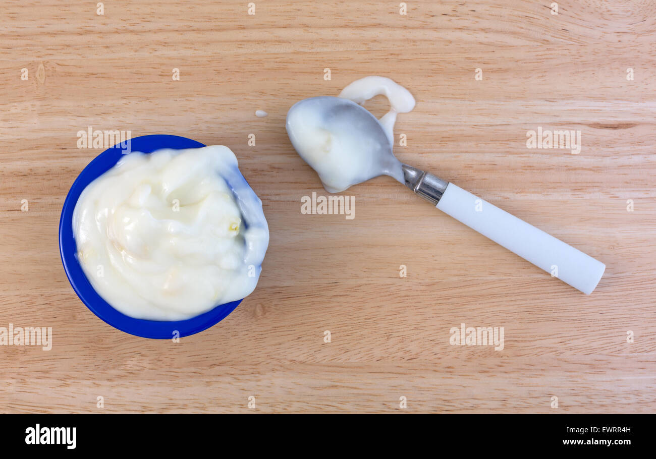 Una piccola ciotola di colore blu con un serving di ananas yogurt più un cucchiaino di colore bianco al lato con una porzione versato su una tavola di legno alto. Foto Stock