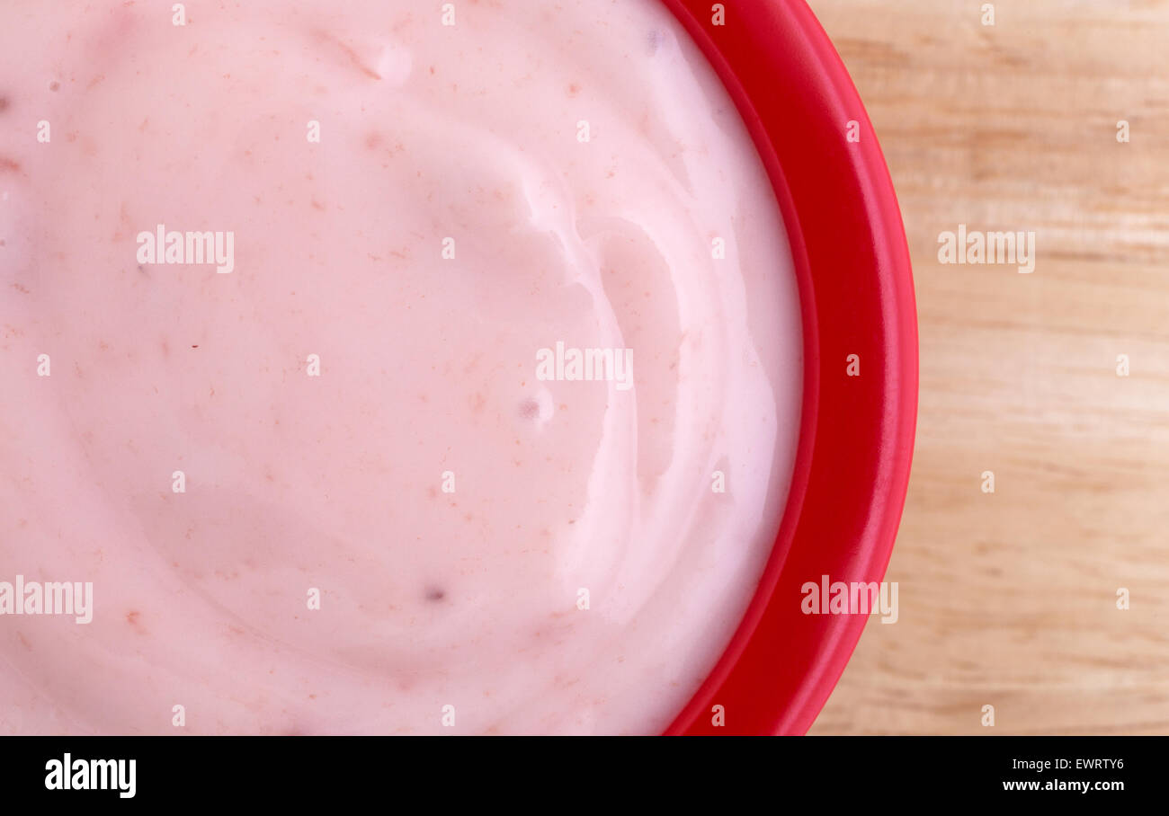 Molto vicino in vista di una piccola dose di crema di yogurt alla fragola in un recipiente rosso sulla parte superiore di una tavola di legno top illuminato da vincere Foto Stock