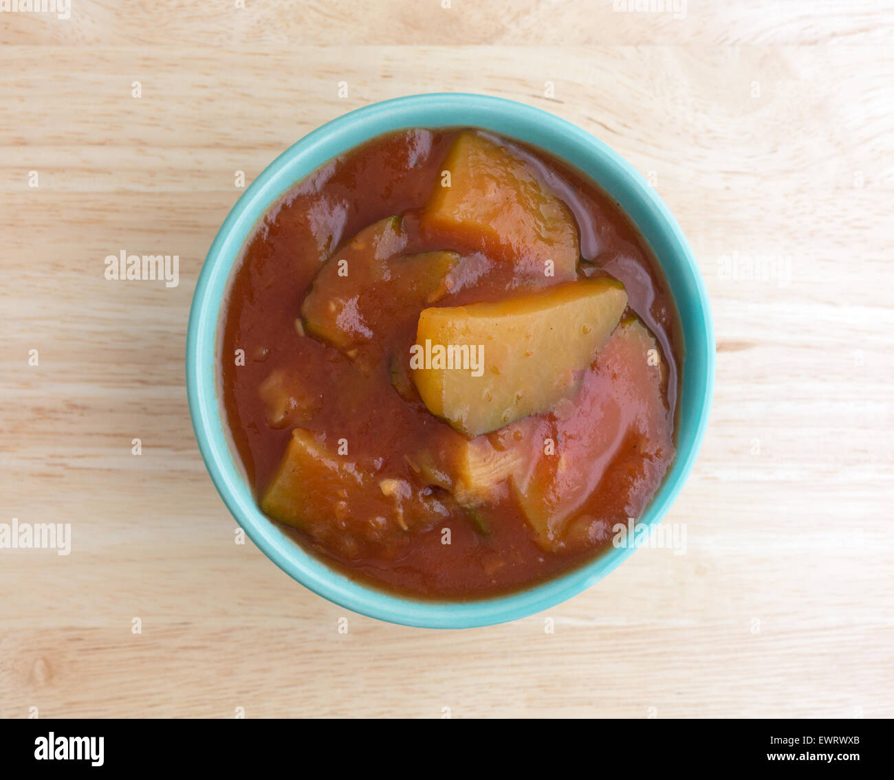 Vista dall'alto di una piccola ciotola riempita con zucchini cotto in una salsa di pomodoro su una tavola di legno top illuminati dalla luce della finestra. Foto Stock