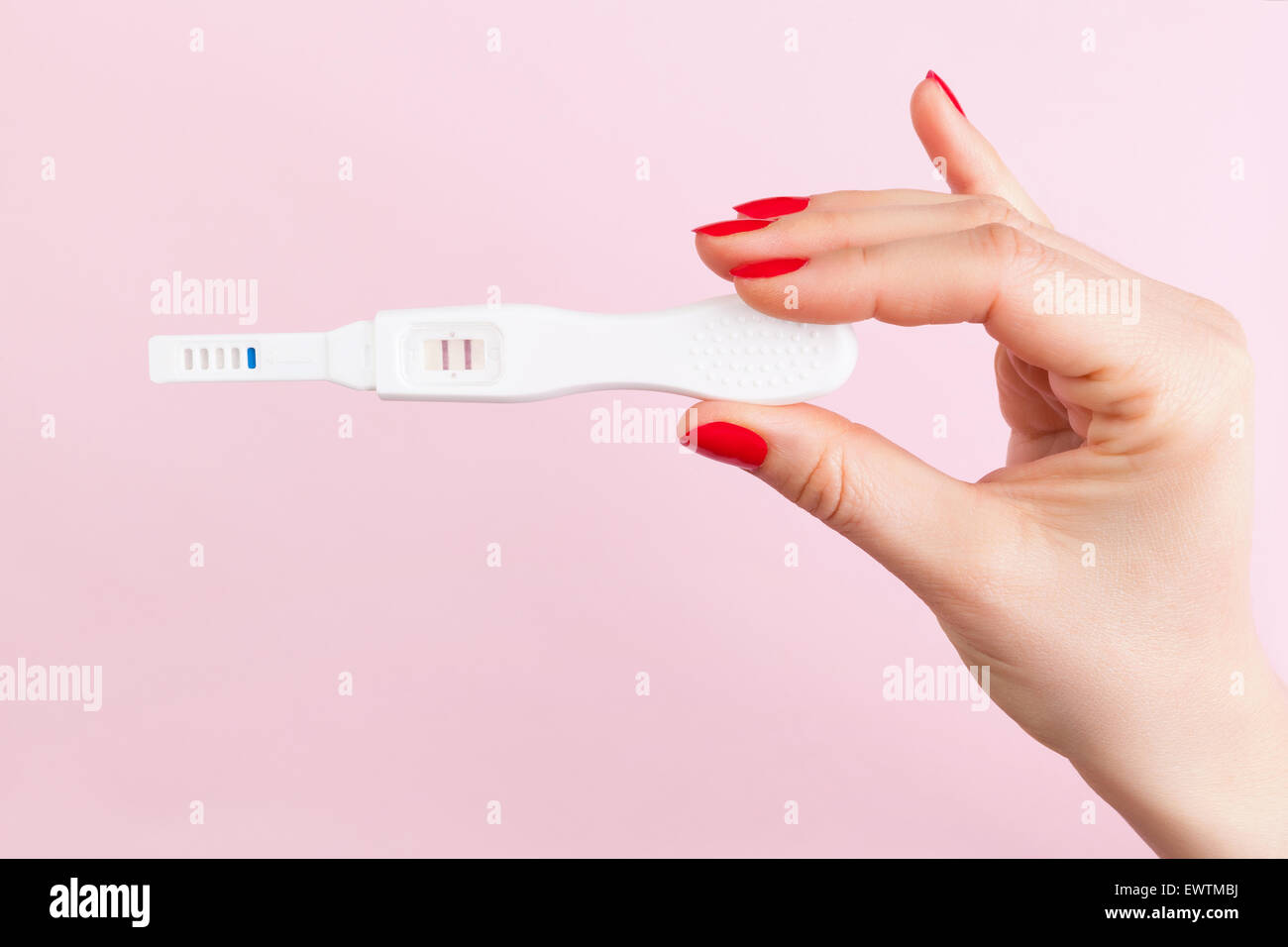 Bella mano femminile con le unghie rosse azienda positivi ai test di gravidanza isolato su sfondo rosa. La maternità, la gravidanza Foto Stock
