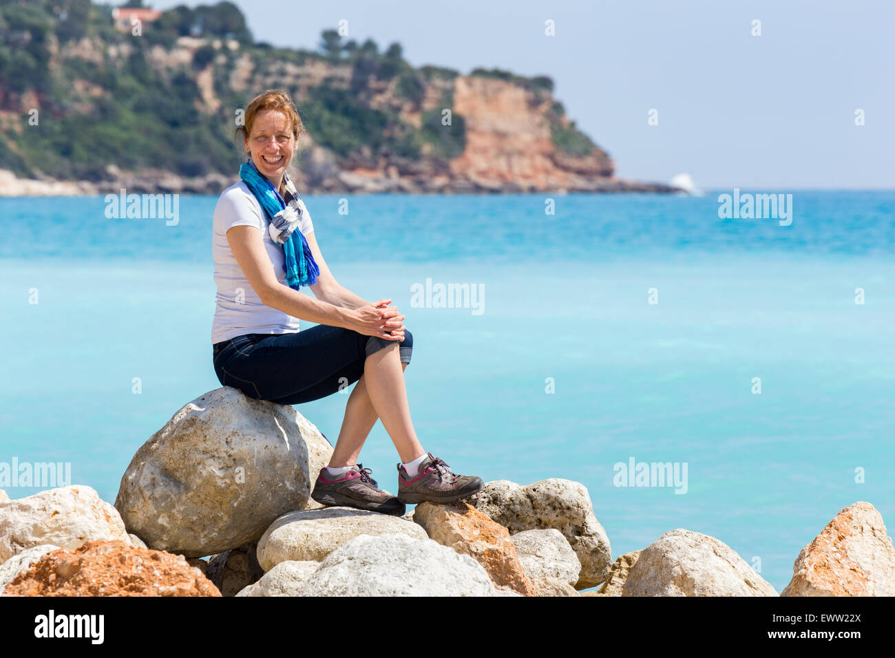 Caucasian donna di mezza età come turista seduta sulle rocce vicino al mare blu godendo di vacanza Foto Stock