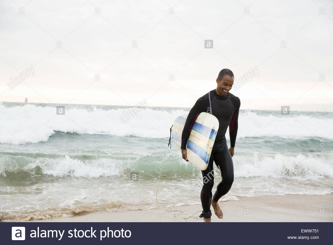 Uomo in neoprene con la tavola da surf a piedi da Ocean Foto Stock