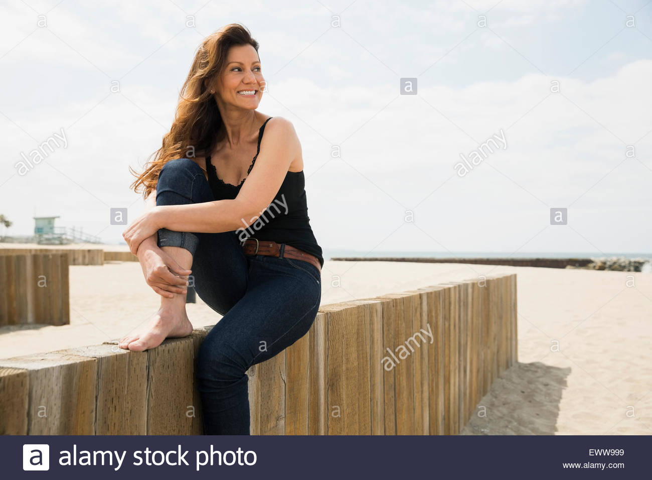Sorridente a piedi nudi donna seduta sulla parete di spiaggia Foto Stock