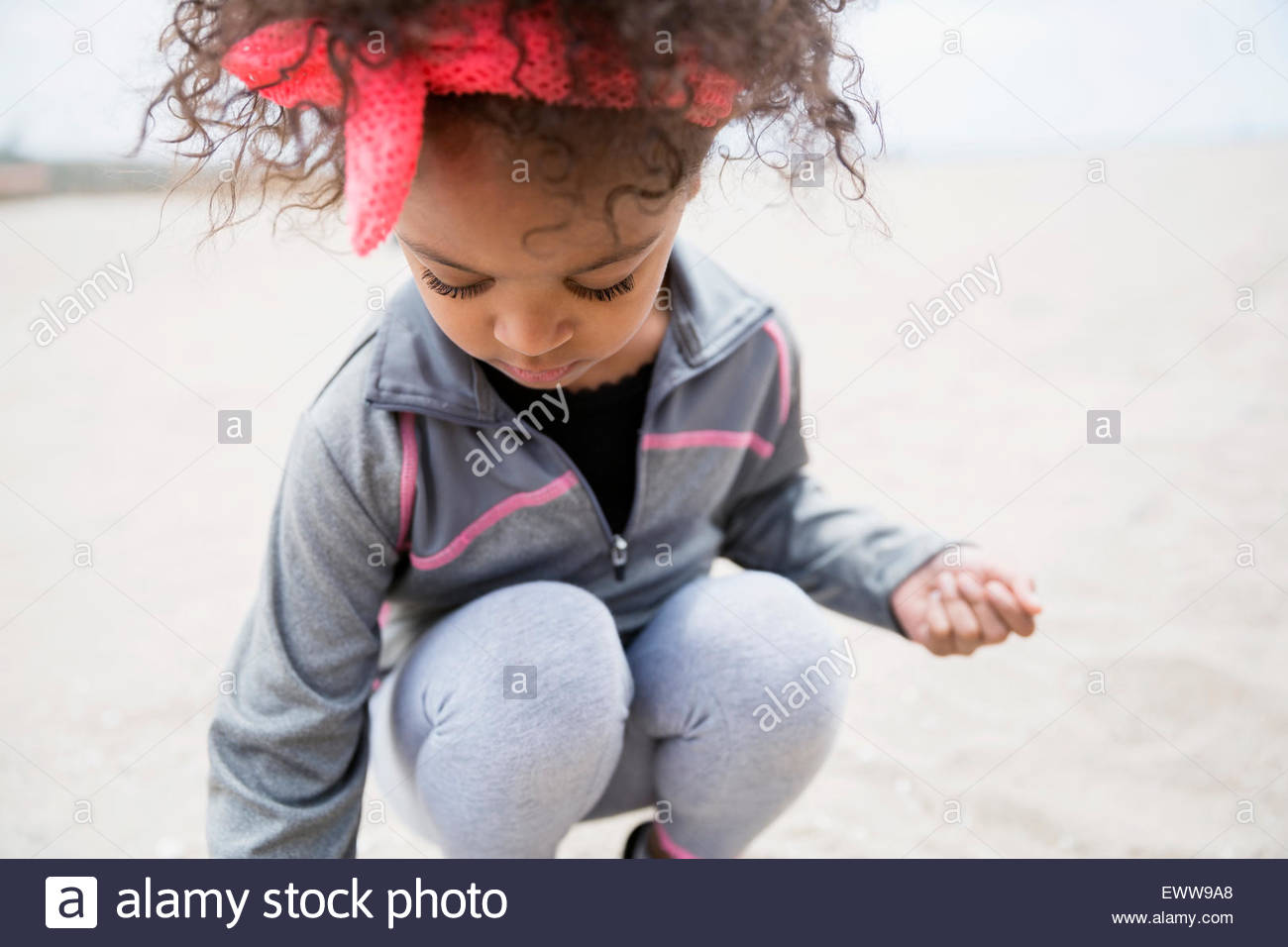 La ragazza con i capelli ricci accovacciato sulla spiaggia Foto Stock