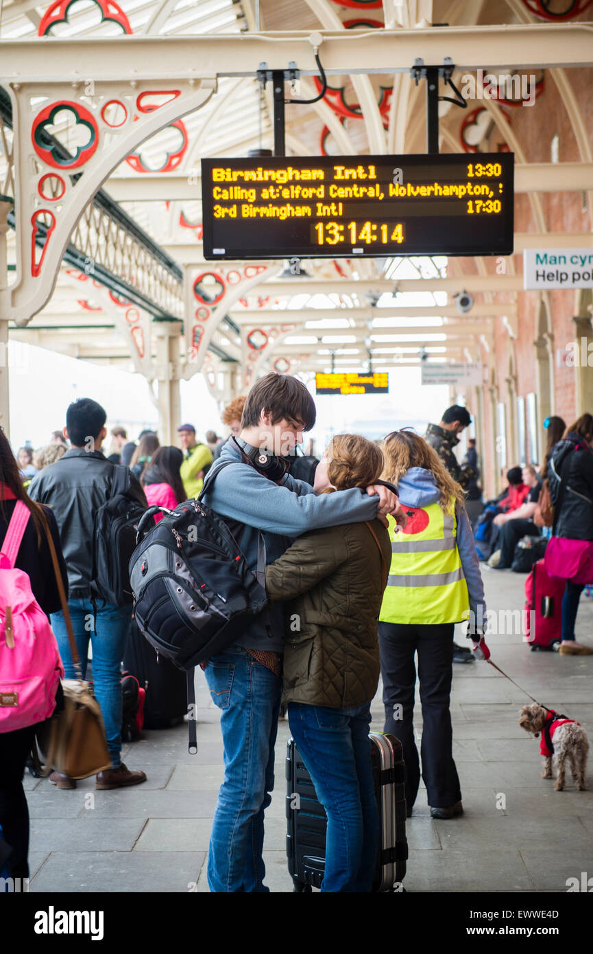 Tornando a casa per l'estate: una coppia giovane ragazzo Ragazza donna uomo gli studenti universitari abbracciano attendere il loro treno sulla piattaforma affollato alla fine dell'anno accademico : Aberystwyth stazione ferroviaria, Wales UK Foto Stock