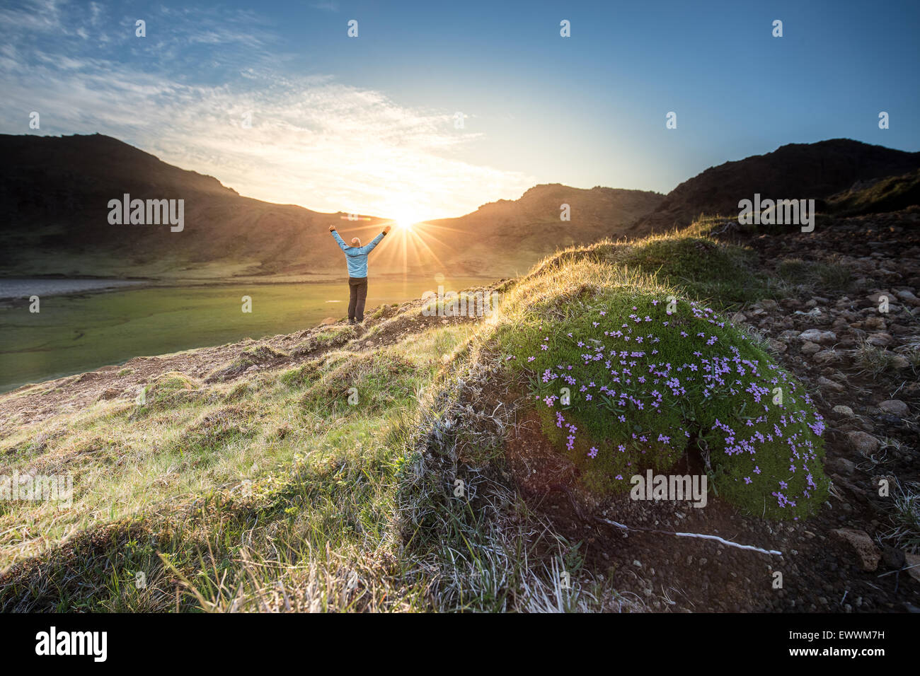 Uomo che indossa blue shell jacket celebrando il tramonto dopo una escursione in montagna, il sole tramonta dietro una catena montuosa, e l'ultimo Foto Stock