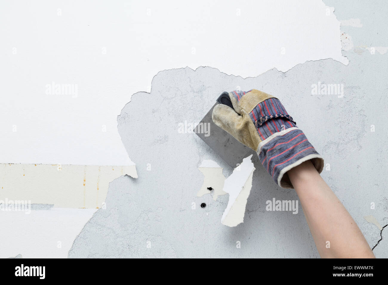 Persona di raschiatura della vernice bianca del muro di cemento durante un home progetto di ristrutturazione Foto Stock