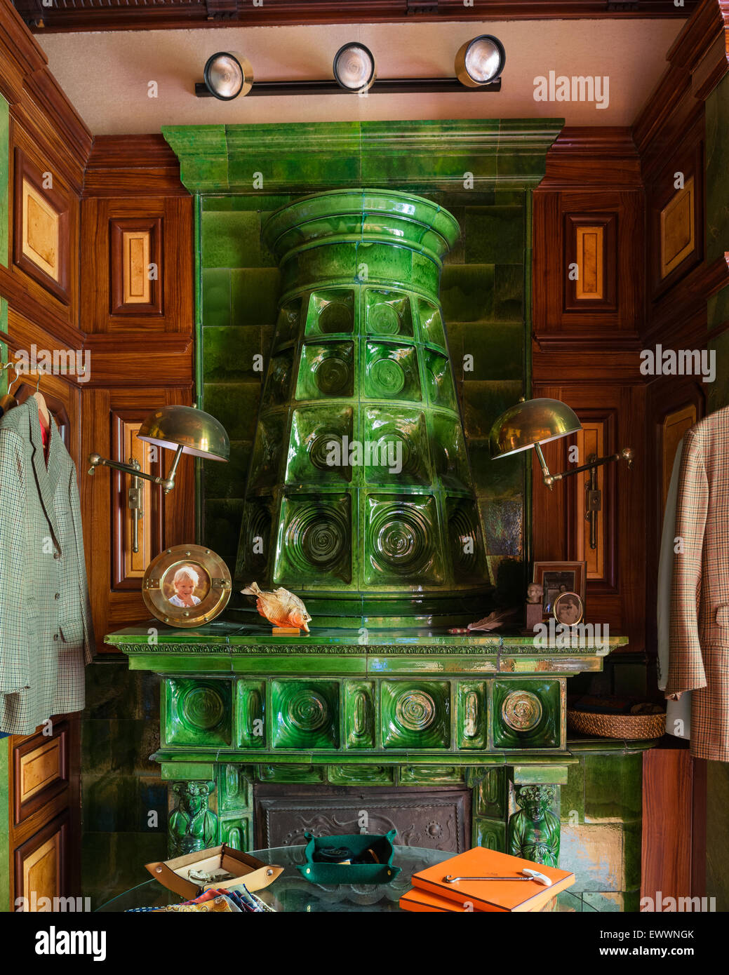 Green stufa in maiolica in studio con pareti in pannelli di legno e ottone e luci a parete Foto Stock