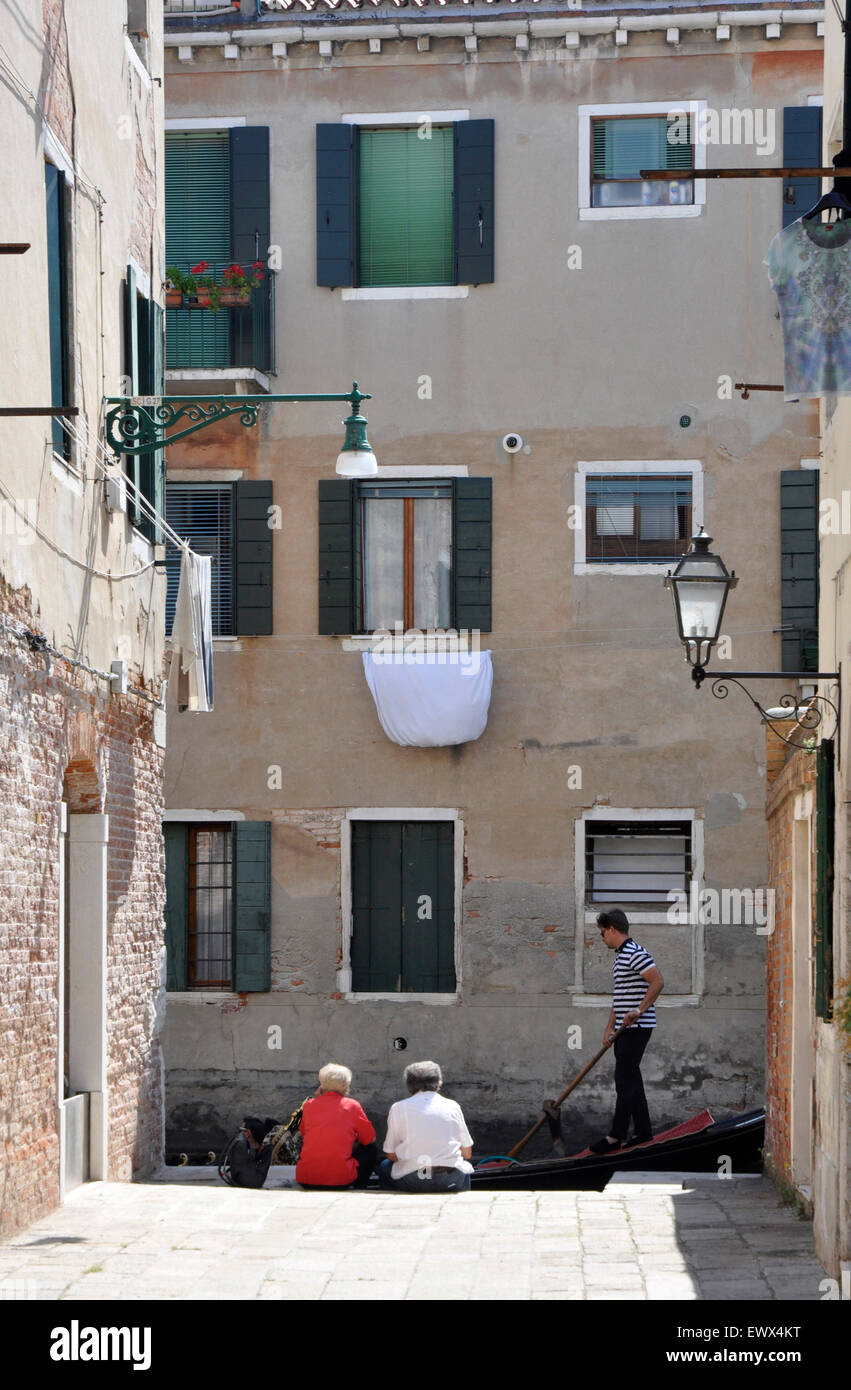 Italia Venezia - strada laterale - backwaters canal zona Santa Croce - giovane seduto - passando gondola - case alte - ombre Foto Stock