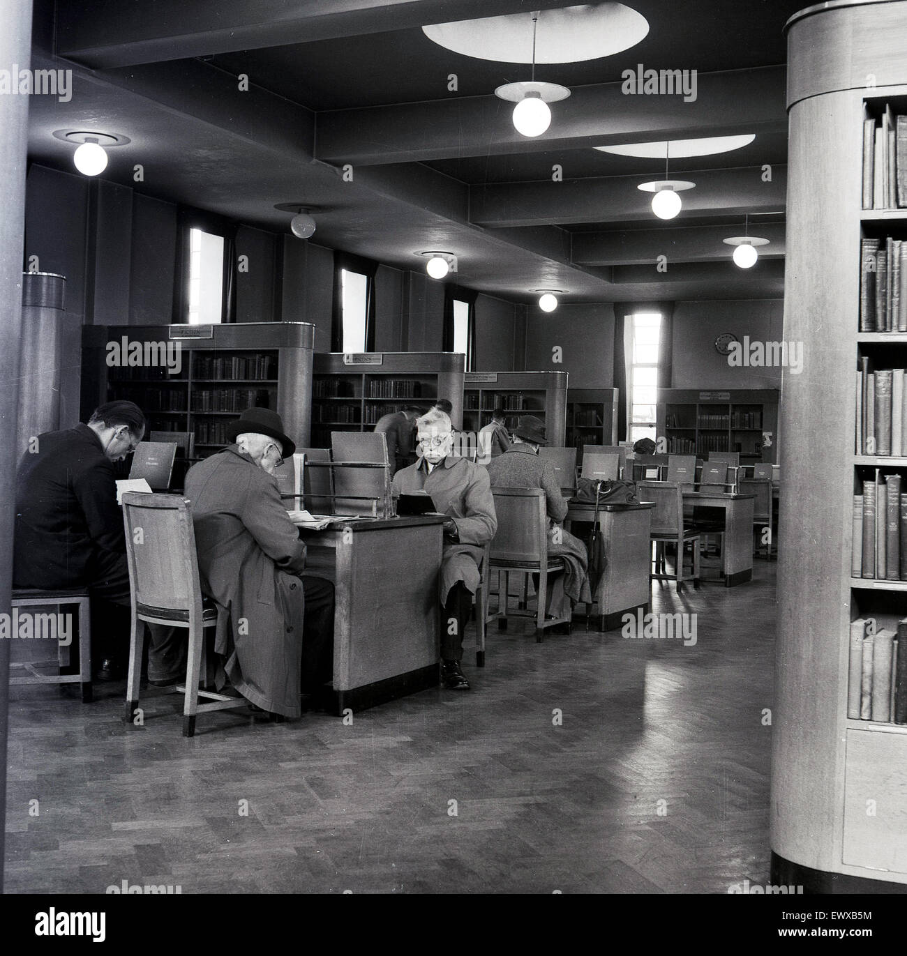 1950s, storico, un certo numero di Signore più anziani, alcuni in cappotti lunghi, seduti alle scrivanie in una biblioteca pubblica, Reading, Inghilterra, Regno Unito. Foto Stock