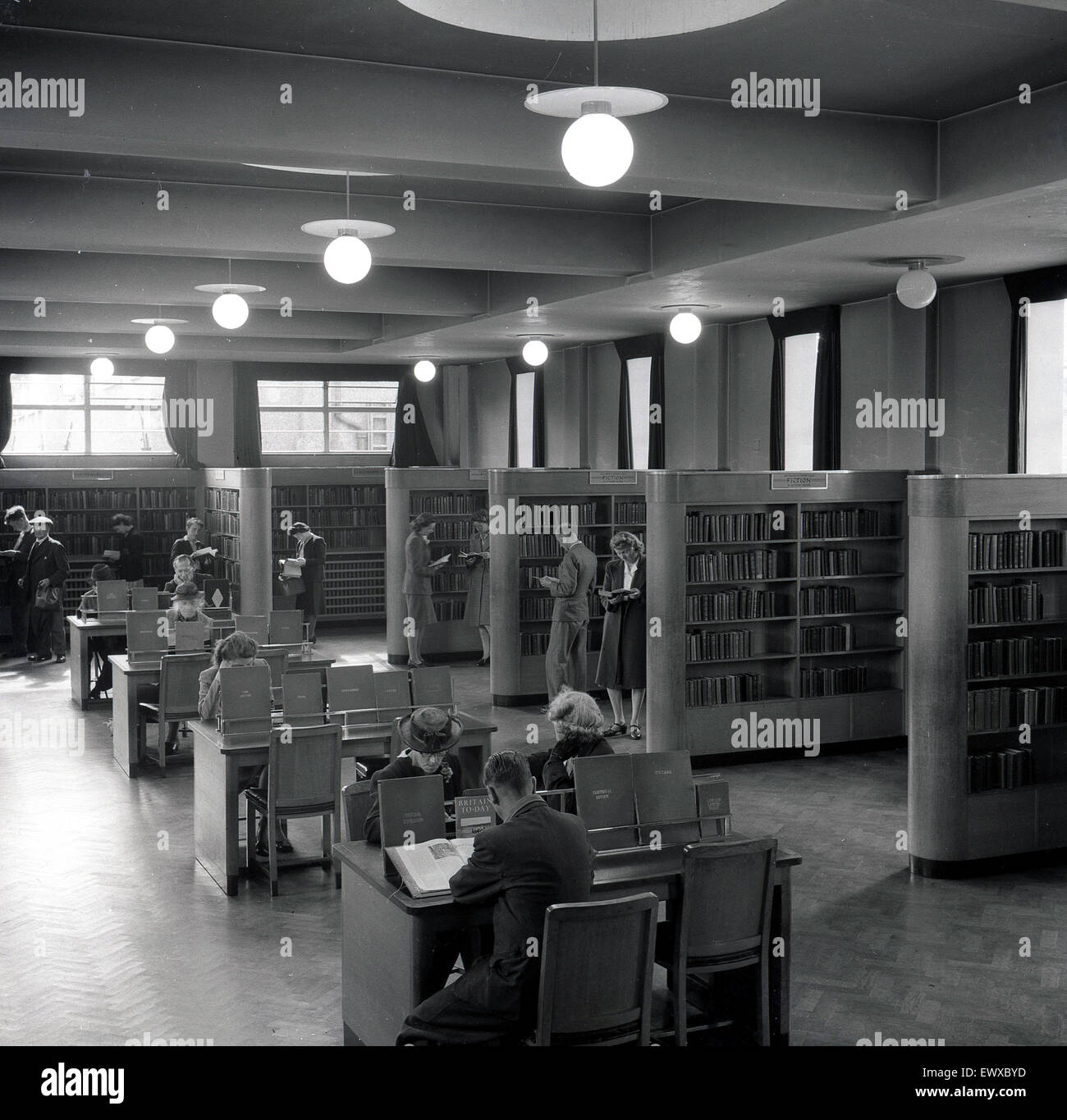 Anni '1950, storico, una vista interna del pavimento di una biblioteca pubblica, Inghilterra, Regno Unito, persone alle librerie e altri seduti a leggere e studiare libri alle scrivanie di legno nel centro. Foto Stock