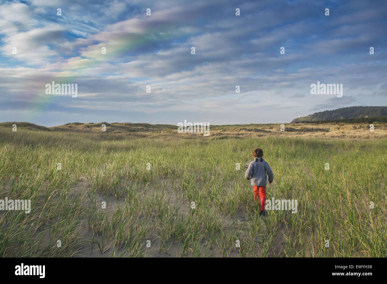 Vista posteriore di un ragazzo che corre attraverso le dune di stand di arcobaleno nel cielo Foto Stock