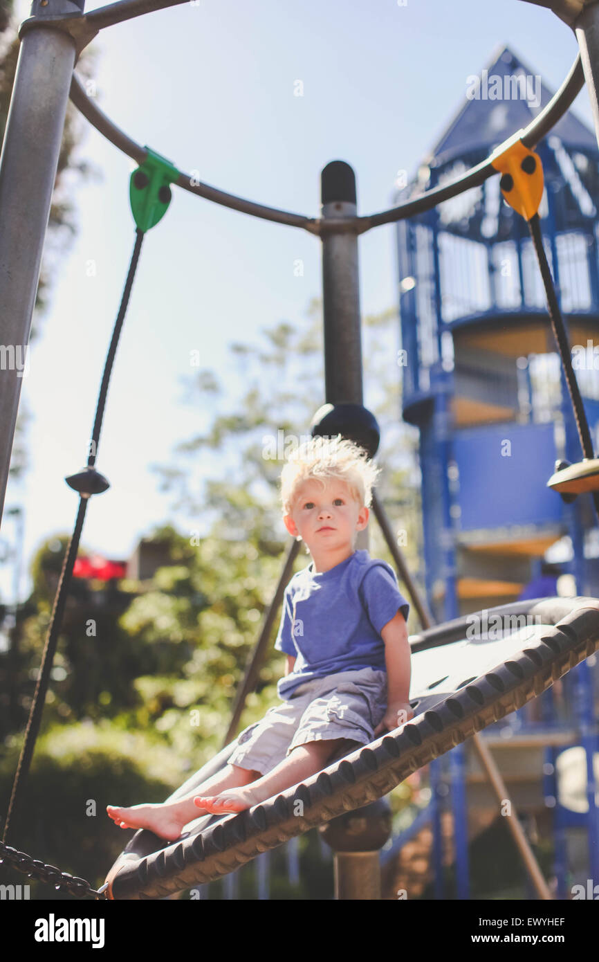 Ragazzo presso il parco giochi seduto ona swing Foto Stock
