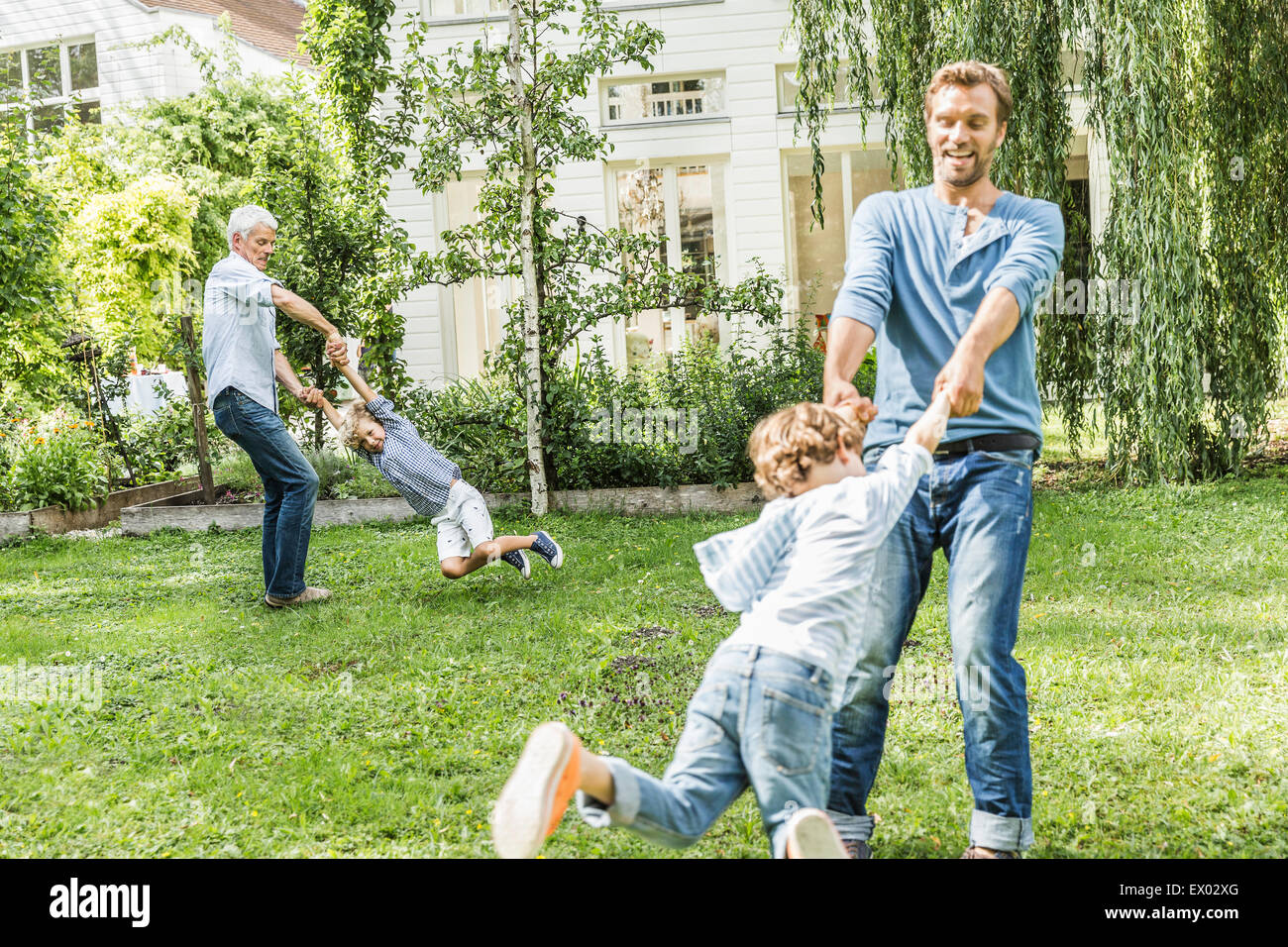 Metà uomo adulto con padre giocando oscilla con figli in giardino Foto Stock