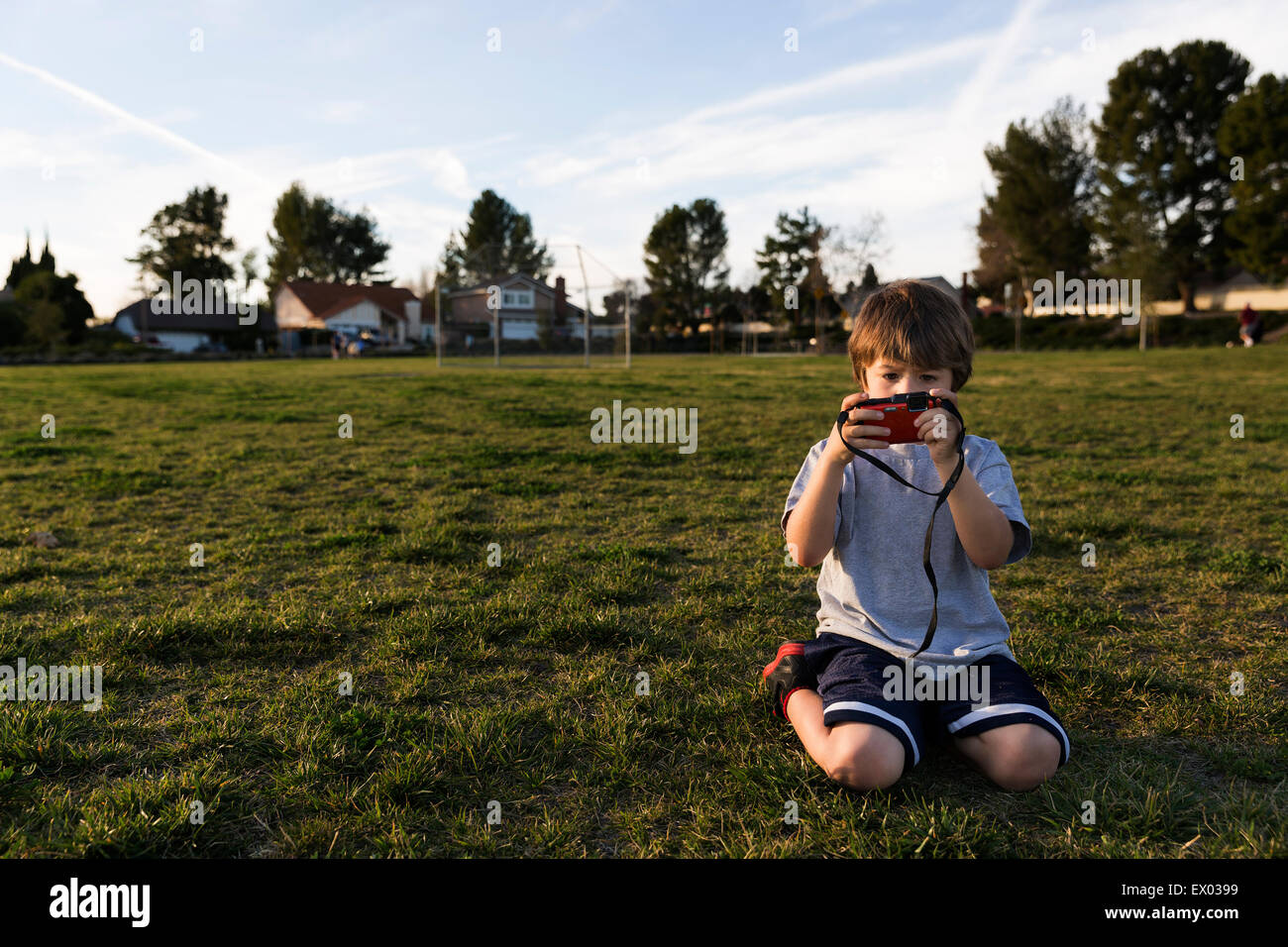 Ragazzo in ginocchio in park guardando la fotocamera digitale Foto Stock