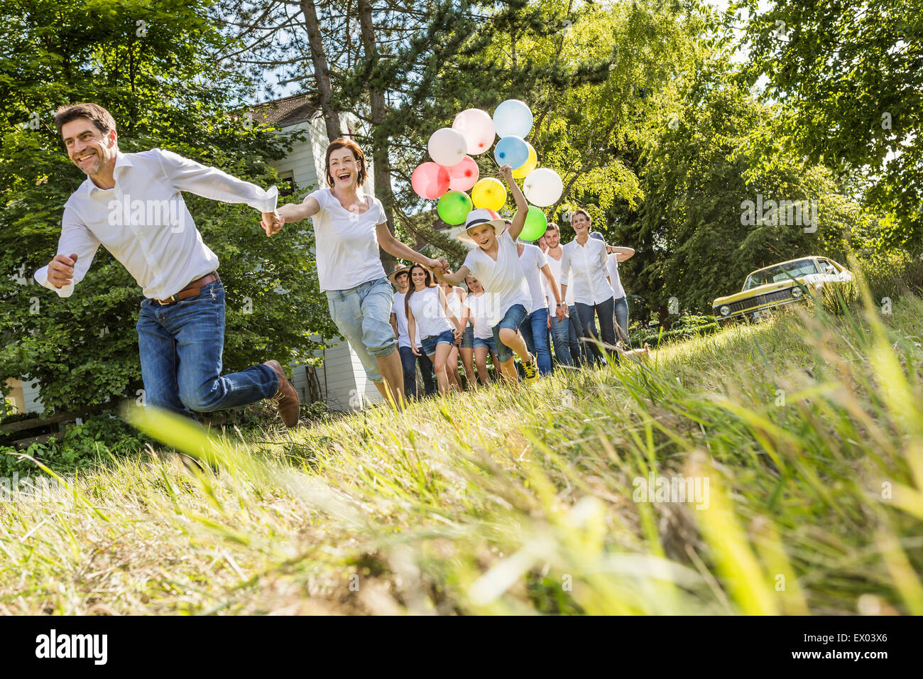 Gruppo di persone che corre attraverso la foresta, boy holding mazzetto di palloncini Foto Stock
