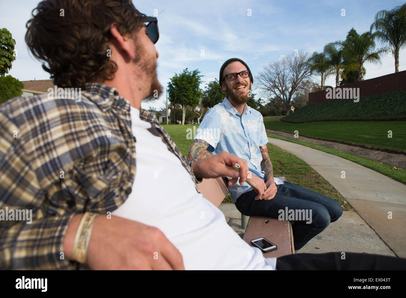 Due maschi giovani amici chattare su banco suburbana Foto Stock