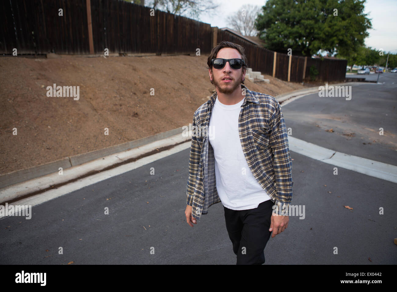 Giovane maschio hipster guardando la fotocamera mentre si camminava sulla strada suburbana Foto Stock