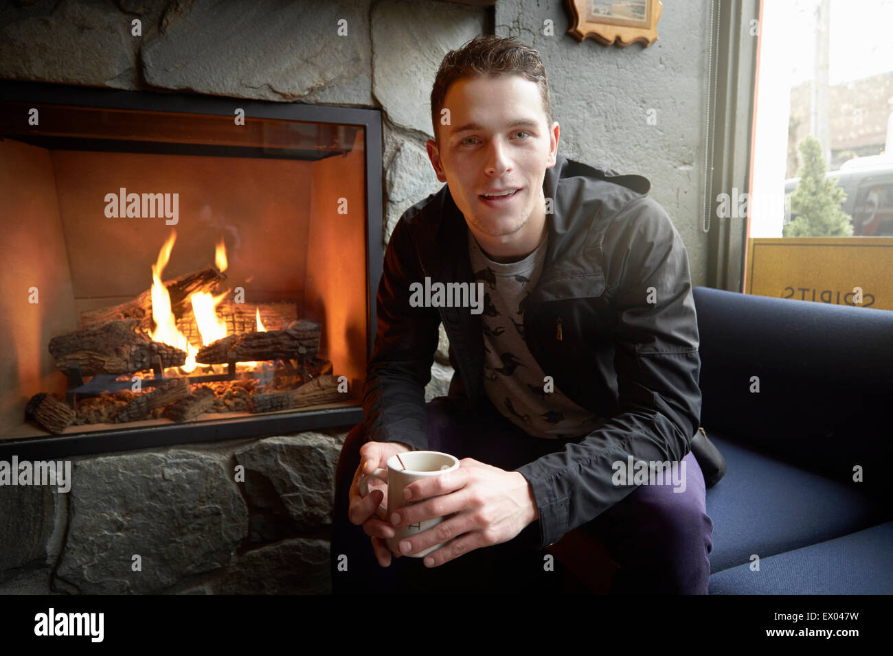 Ritratto di giovane uomo seduto da aprire il fuoco in cafe Foto Stock