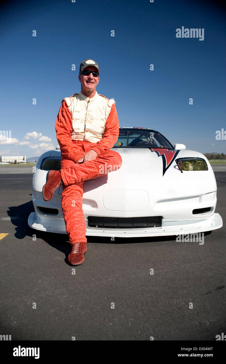 Ritratto di maschio maturo racing auto conducente appoggiata contro la vettura da corsa Foto Stock