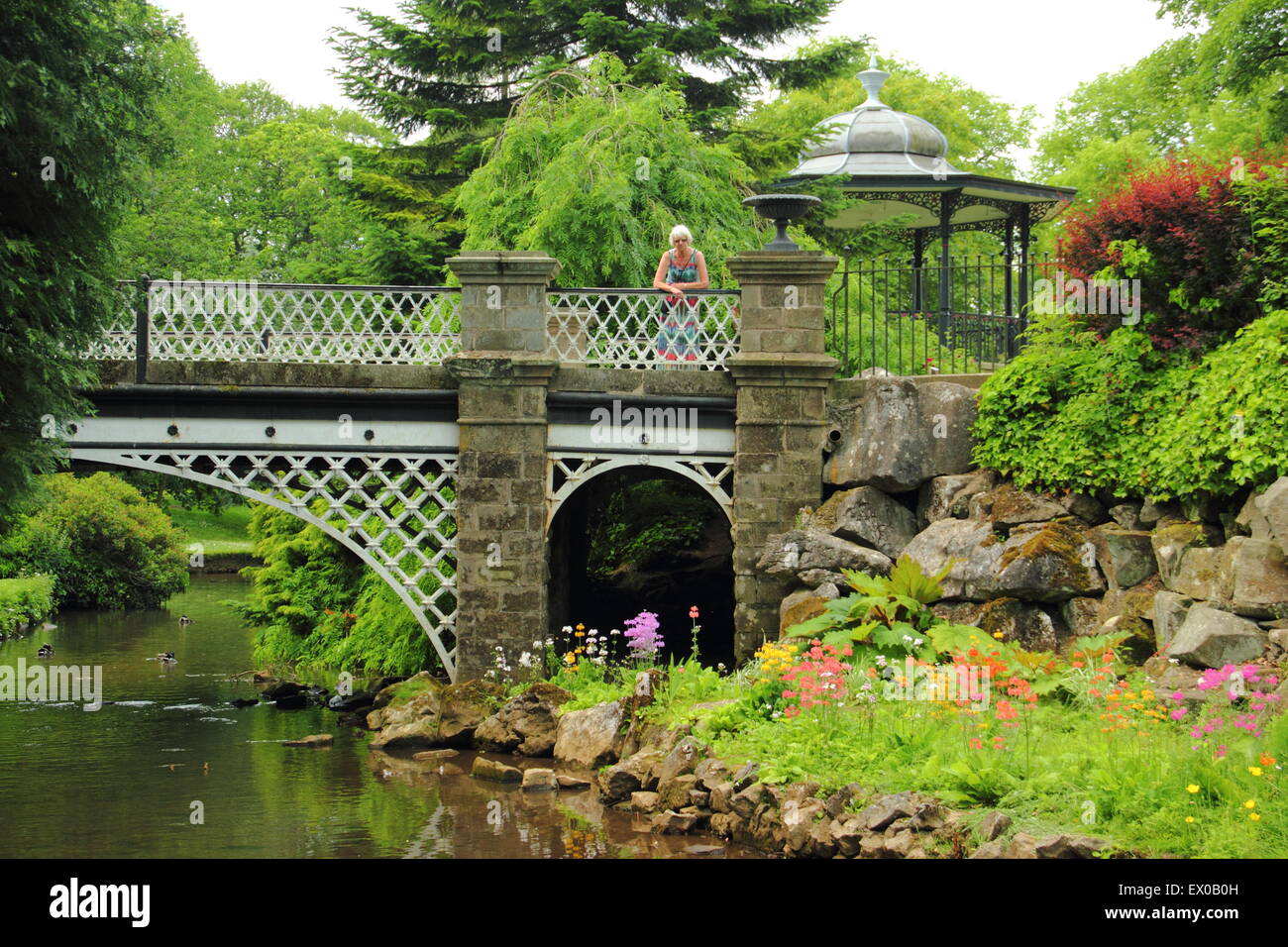 Una donna mette in pausa su un ponte vicino al palco per spettacoli (foto) nel Pavilion Gardens in Buxton Derbyshire Inghilterra - estate 20 Foto Stock