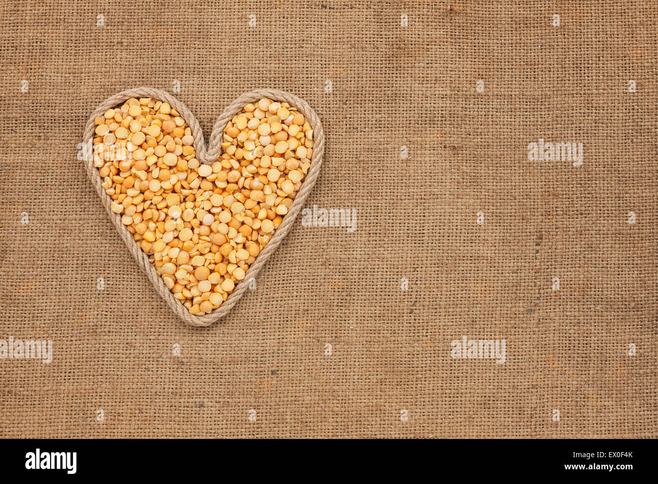 Cuore realizzato dalla corda con piselli secchi giacente su un letto di sacco, con spazio per il testo Foto Stock