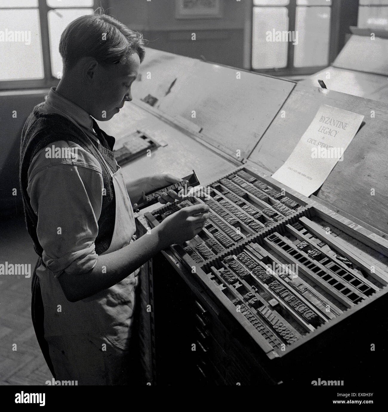 anni '1950, storico, l'immagine mostra un giovane tipografo. Sta cercando il tipo fisico, le lettere e i simboli chiamati Sort, che corrispondano al testo sulla carta, il titolo del libro, The Byzantine Legacy, di Cecil Stewart. Foto Stock