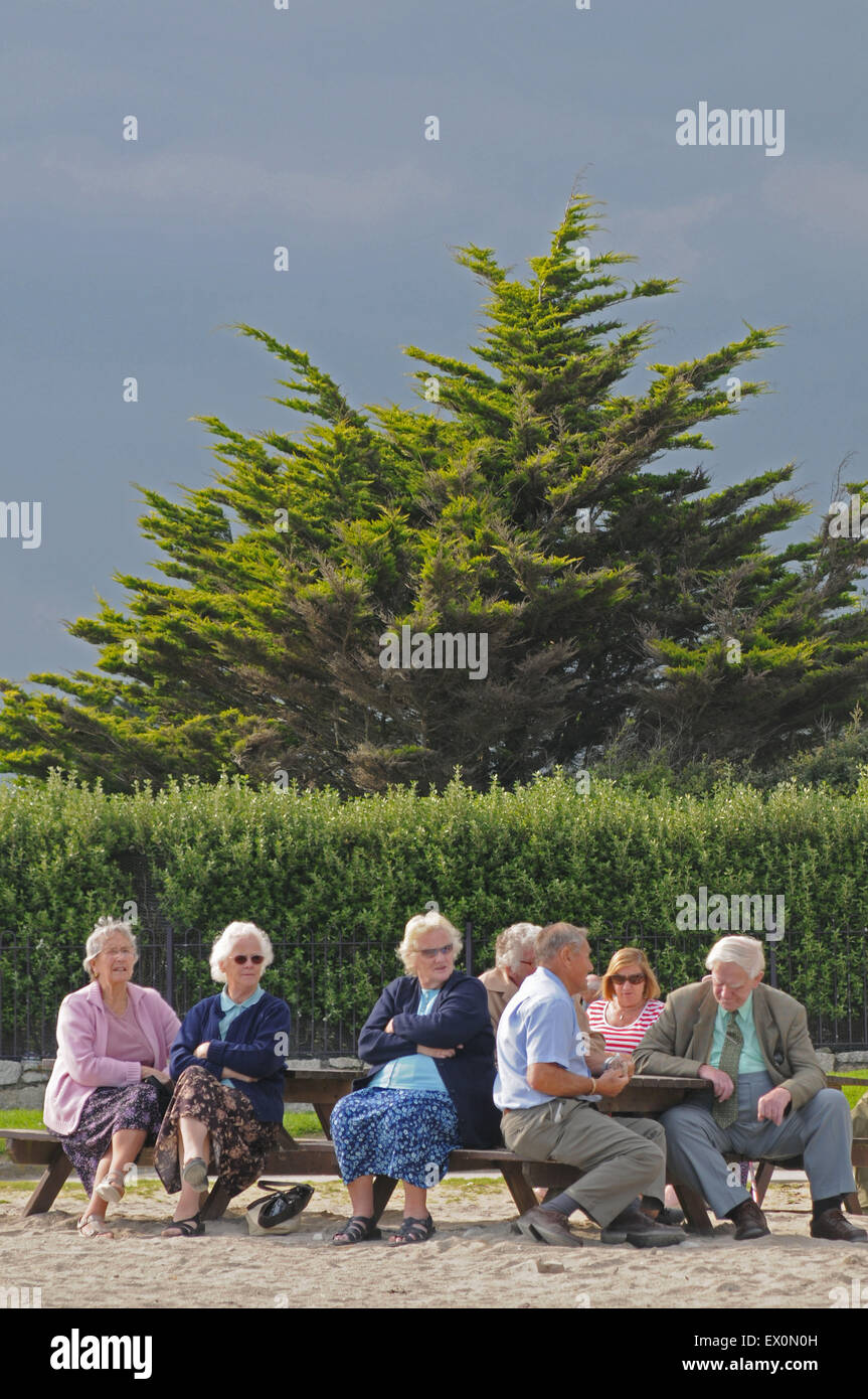 Un gruppo di persone anziane siedono su sedili in corrispondenza del bordo della spiaggia di Falmouth, Regno Unito. Foto Stock