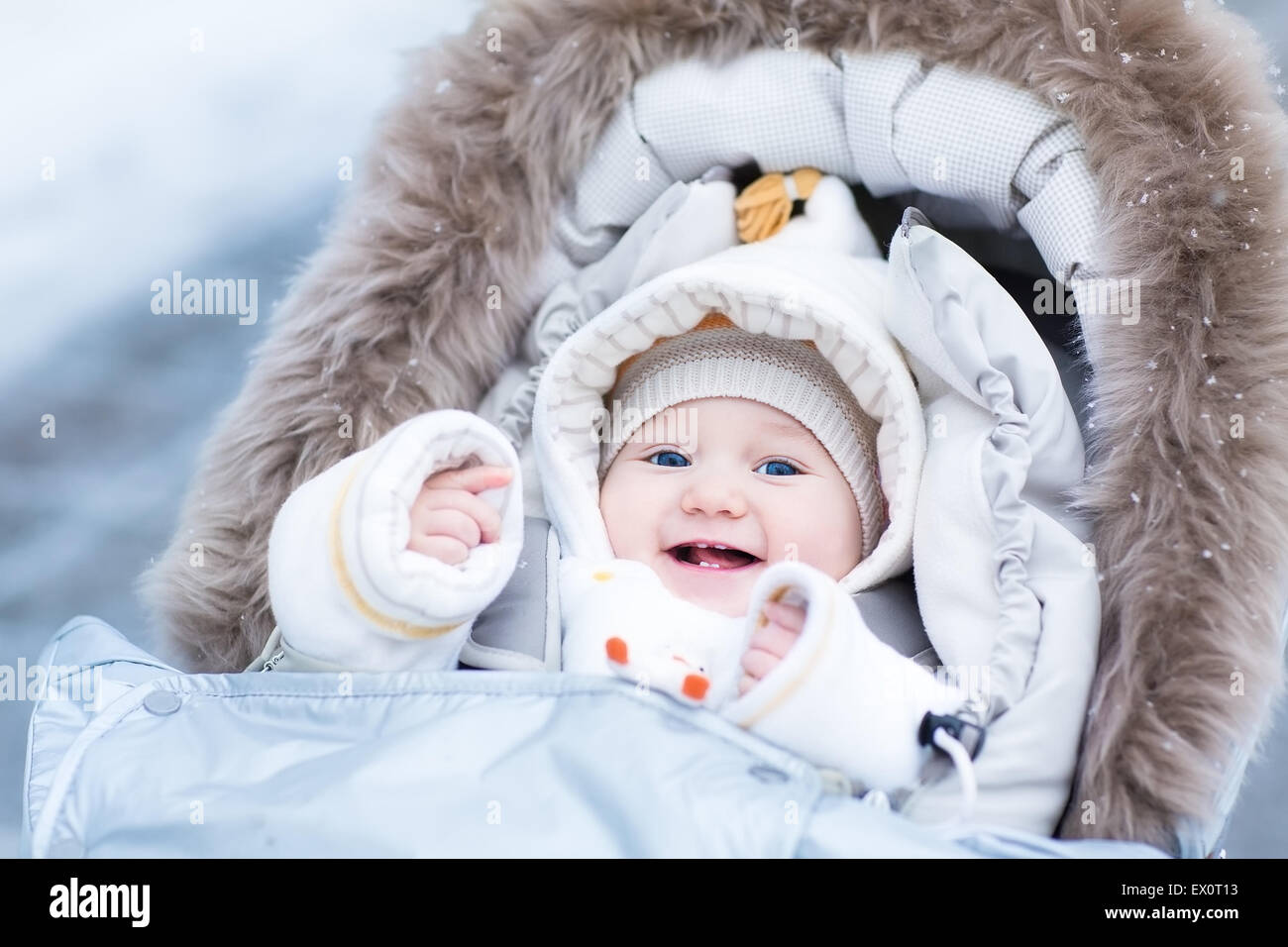 Happy Laughing baby girl godendo di una passeggiata in un inverno nevoso park seduto in un caldo passeggino con cappa di pelle di pecora Foto Stock