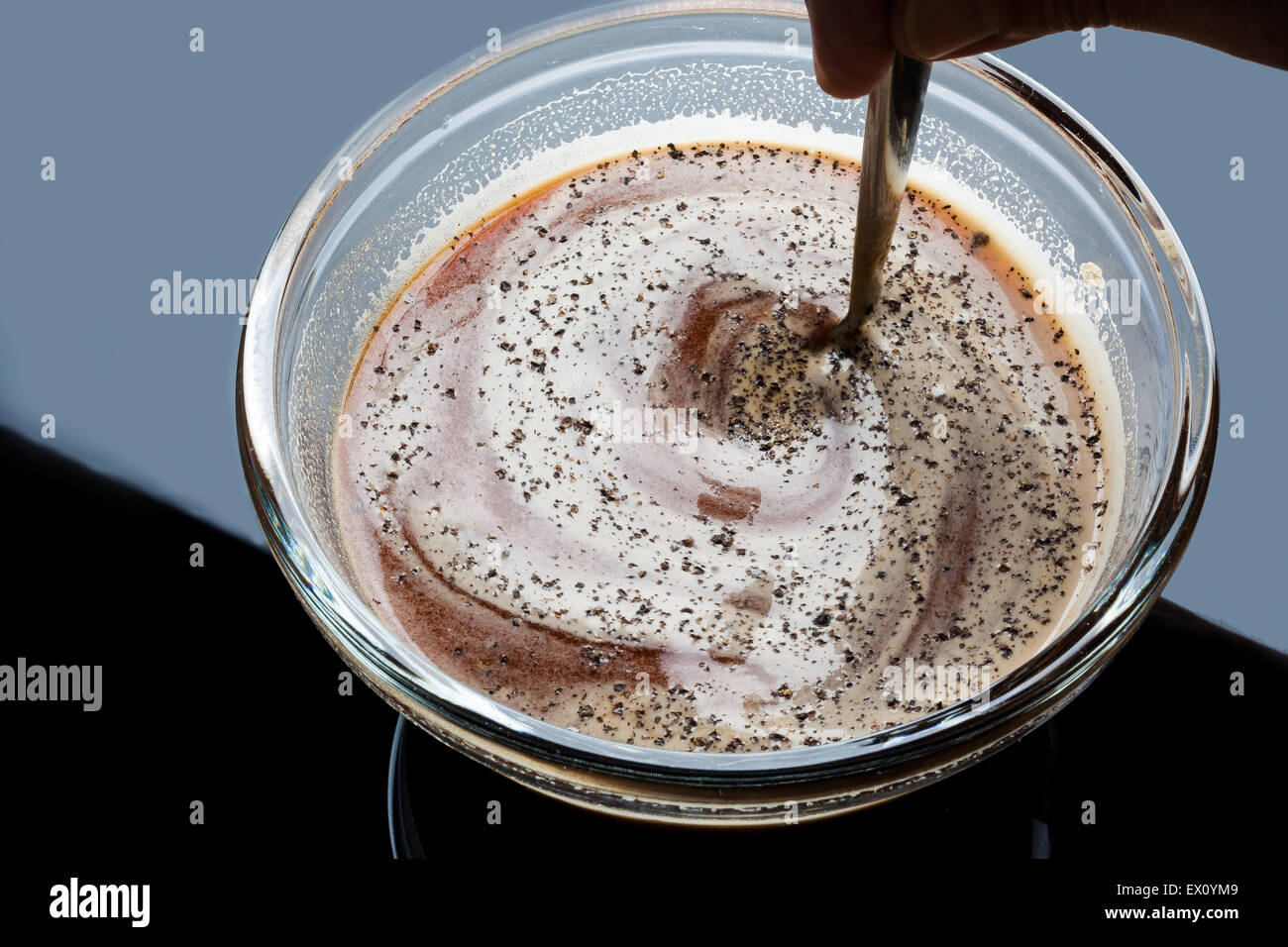 Agitazione la salsa di pomodoro e il pepe nero in una ciotola di vetro con cucchiaino Foto Stock
