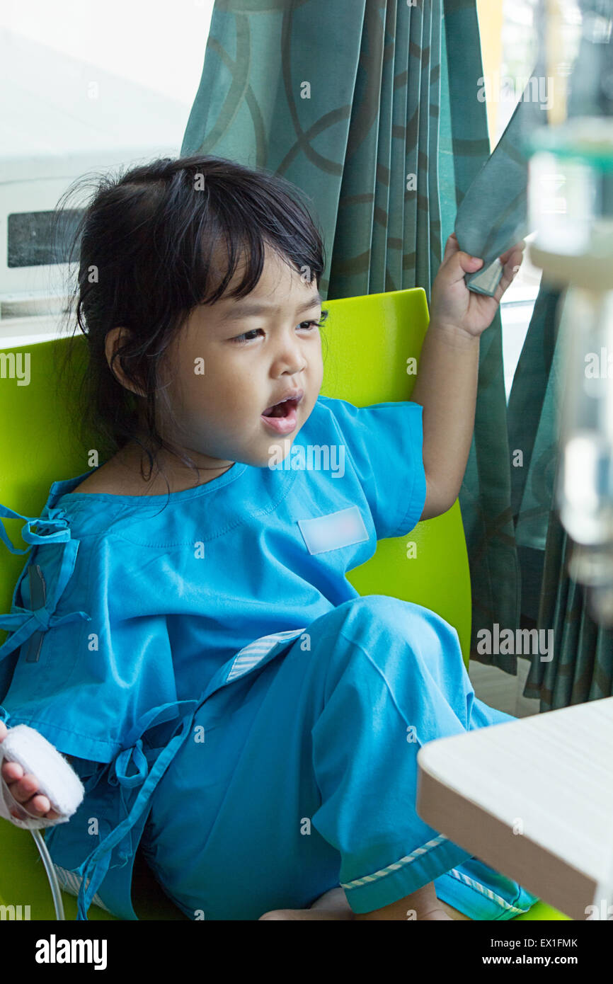 Malattia poco ragazzi asiatici seduto su una sedia in ospedale, soluzione salina per via intravenosa (IV) a portata di mano Foto Stock