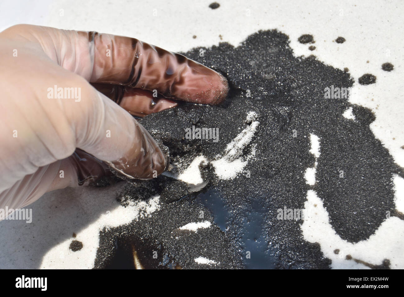 Fuoriuscita di olio sulla sabbia bianca con la mano guantata Foto Stock