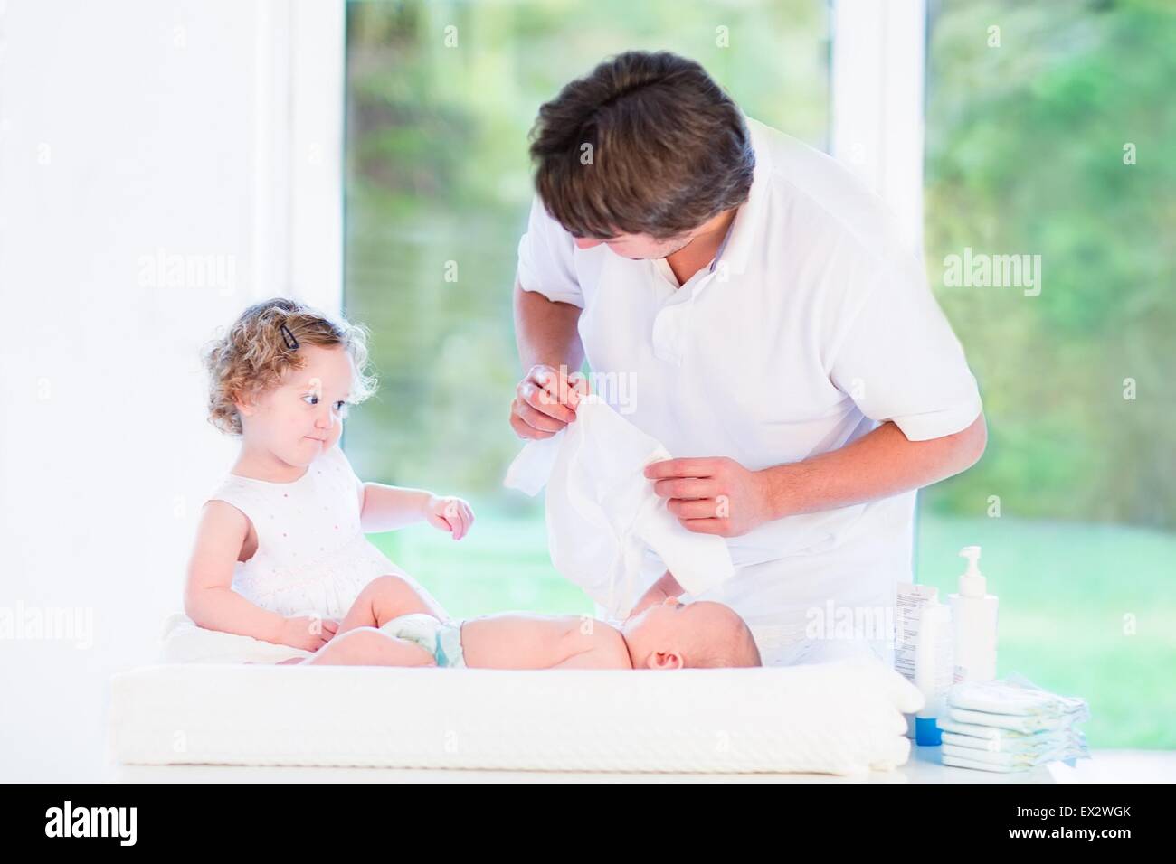 Carino il toddler girl aiutando il padre per cambiare un pannolino e il vestito suo neonato fratello Foto Stock