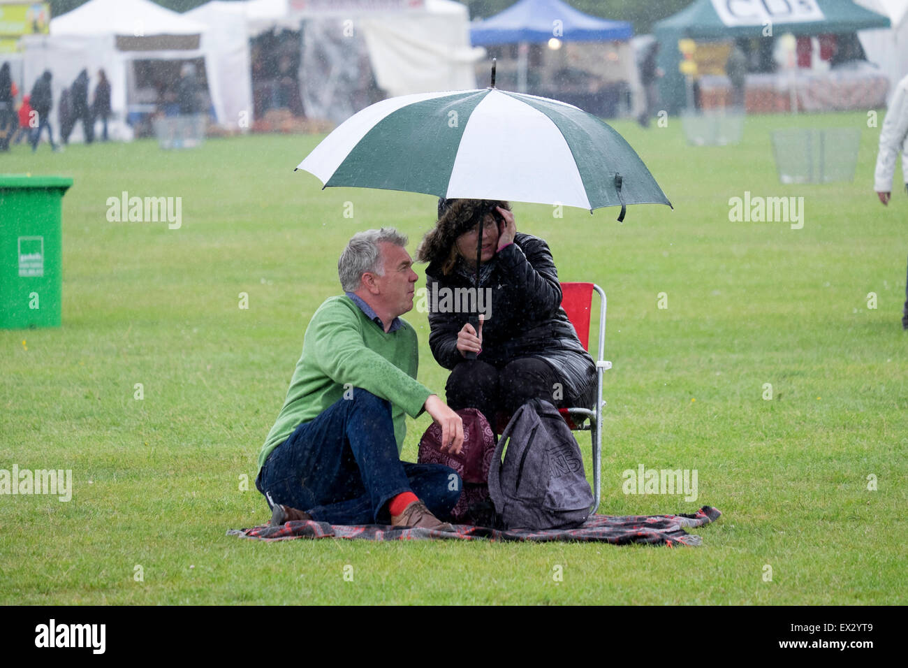 Giovane seduto sotto ombrellone in parco nella pioggia Foto Stock