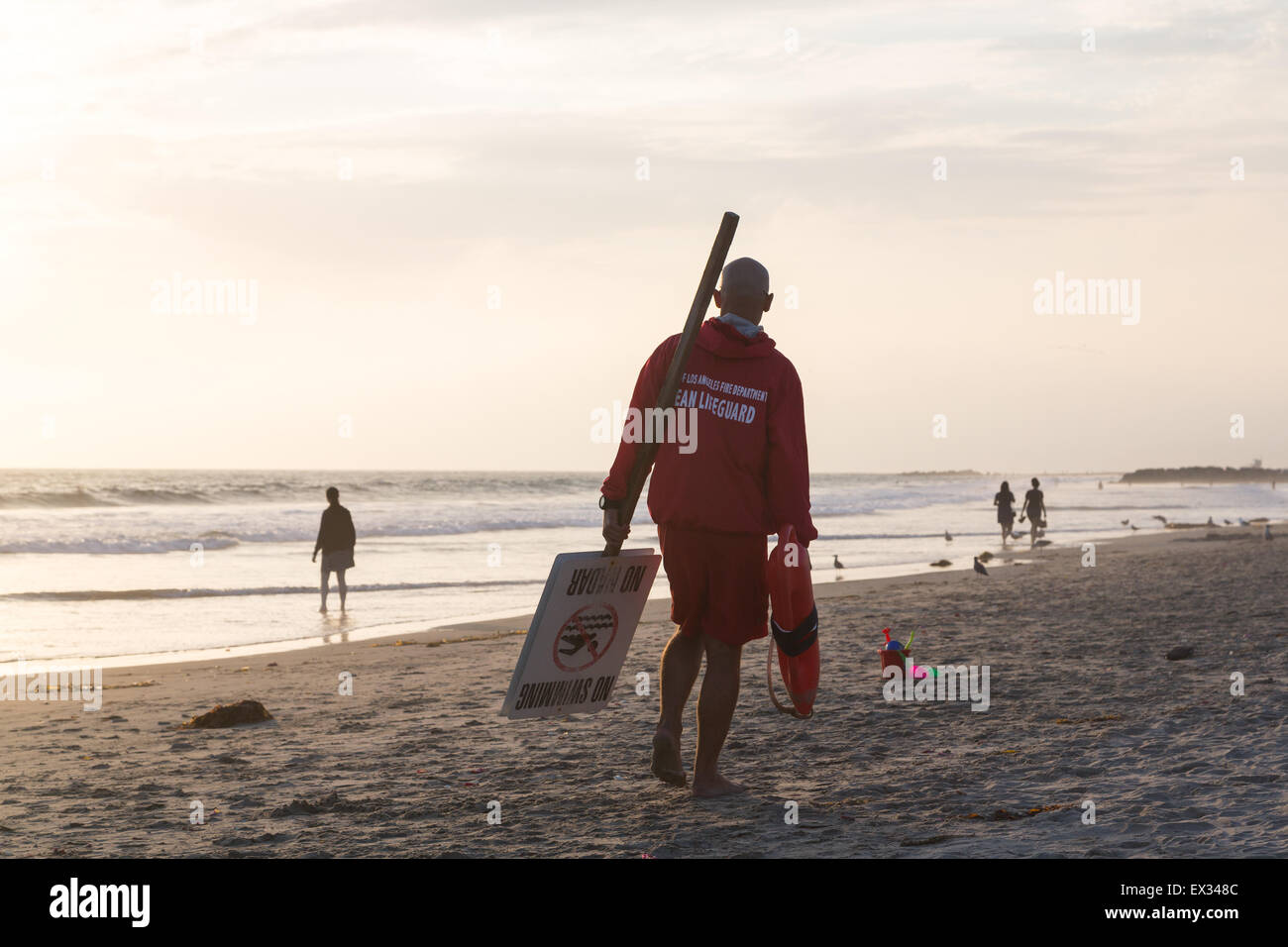 Un bagnino porta un nessun segno di nuoto lungo la spiaggia nel tardo pomeriggio Foto Stock